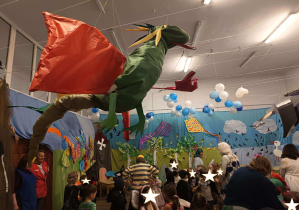 Na pierwszym planielatajacy smok wykonany z kolorowych materiałów: zeliony tułw, czerwone skrzydła.